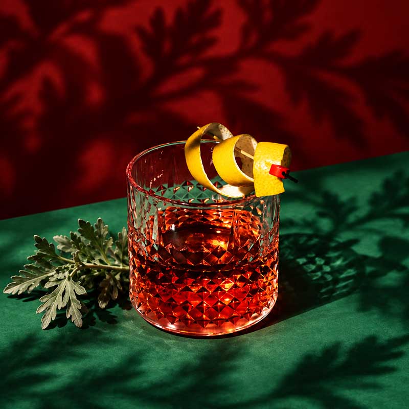 Alt-Text: Sazerac Cocktail mit Zitronenzeste auf grünem Hintergrund